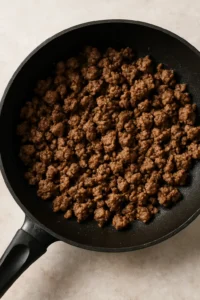 Browning ground beef in a black skillet for beef and pepper rice bowl