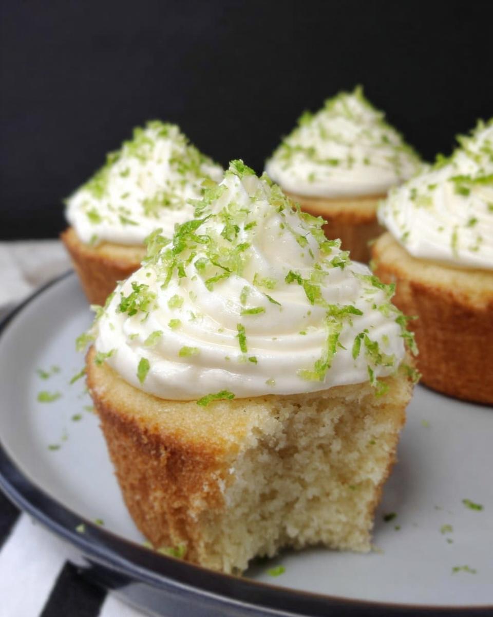 A close-up of a Low Carb Coconut Lime Cupcake with white frosting and lime zest, with a bite taken out.