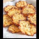 A pile of golden brown, crispy cottage cheese chips sprinkled with sesame seeds.