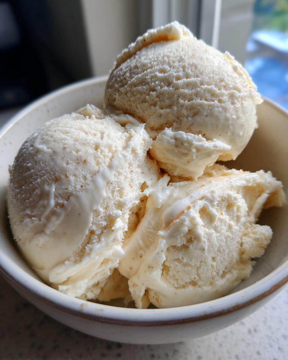 Close-up of three scoops of creamy Easy No Machine Vanilla Ice Cream in a bowl, with visible vanilla bean flecks.