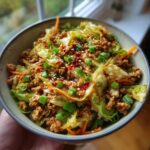 A close-up of a bowl filled with a colorful Egg Roll in a Bowl Recipe, featuring ground meat, cabbage, carrots, and green onions.