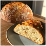 A golden-brown loaf of Garlic Parmesan Artisan Bread, with a slice cut to reveal its airy crumb and cheesy interior.