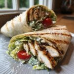 Close-up of two Grilled Lemon Herb Chicken Caesar Wraps filled with sliced chicken, romaine lettuce, and cherry tomatoes.