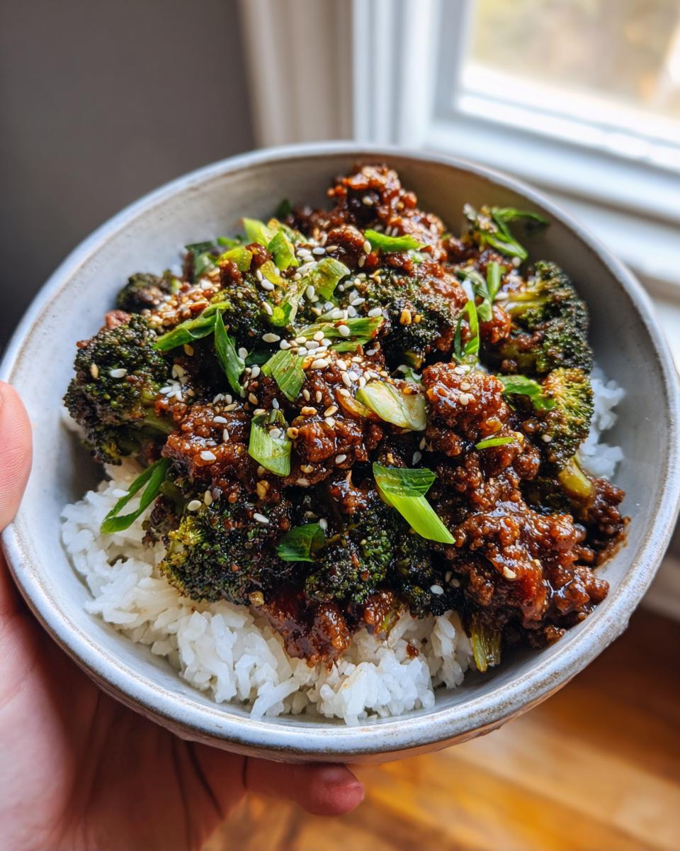 A bowl filled with white rice topped with a savory Ground Beef and Broccoli Dinner Recipe, garnished with sesame seeds and green onions.