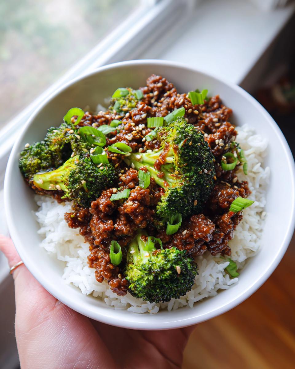 A delicious bowl of Ground Beef and Broccoli Dinner Recipe served over white rice, garnished with green onions and sesame seeds.