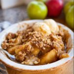 A close-up of a serving of Healthy Apple Crisp topped with two scoops of vanilla ice cream and a spoonful taken out.