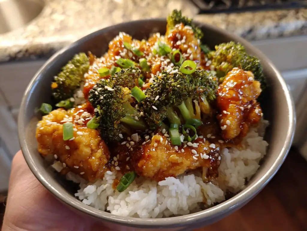 A bowl of Honey Garlic Chicken and Broccoli served over white rice, garnished with sesame seeds and green onions.