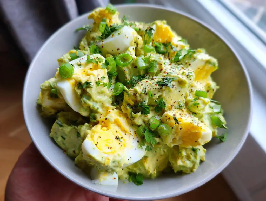 A close-up of a bowl of Keto Avocado Egg Salad, featuring creamy avocado, chopped hard-boiled eggs, and green onions.