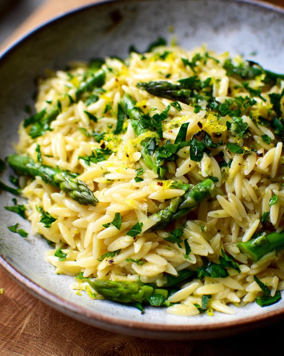 A close-up of a bowl filled with Lemon Asparagus Orzo, garnished with fresh parsley and lemon zest.