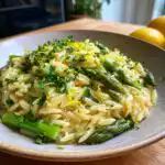 A close-up of a bowl filled with Lemon Asparagus Orzo, topped with fresh parsley and lemon zest.
