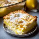 A slice of lemon cream cheese dump cake with a crumb topping, dusted with powdered sugar.