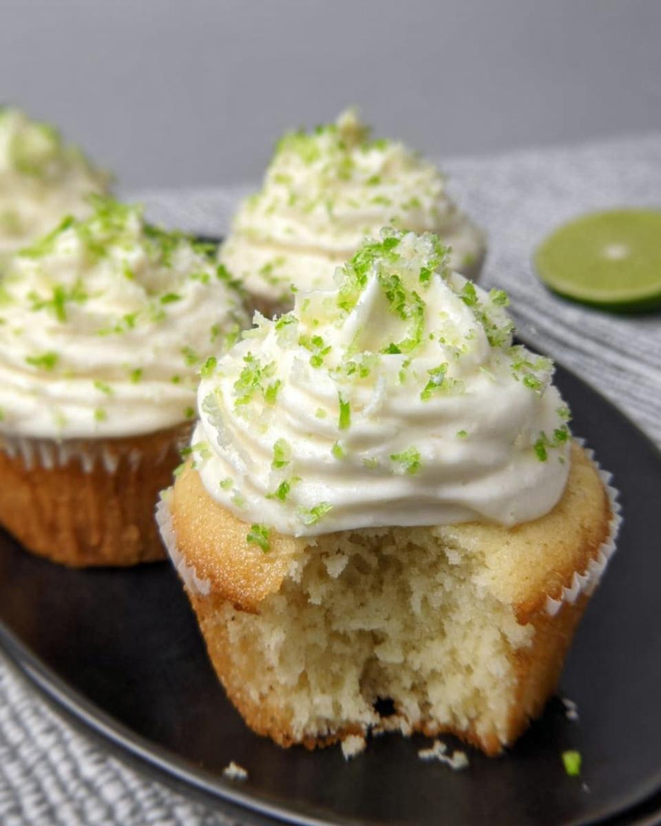 A close-up of a low carb coconut lime cupcake with creamy frosting and lime zest, with a bite taken out.
