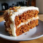 A tempting slice of Moist Carrot Cake with Cream Cheese Frosting, topped with walnuts.