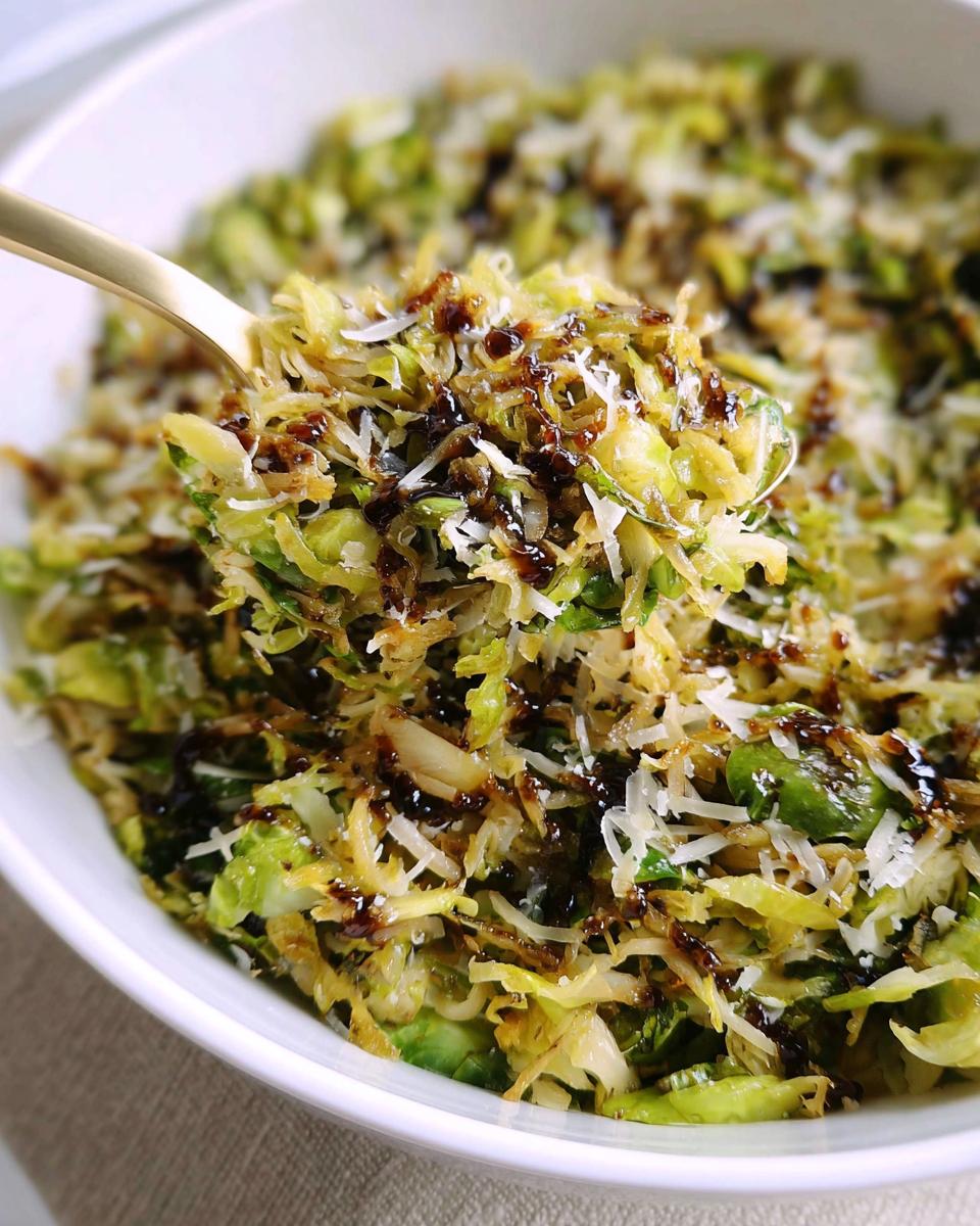 A spoonful of shredded brussels sprouts topped with parmesan cheese and a balsamic glaze.