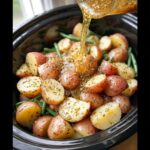 Pouring dressing over halved red potatoes and green beans in a slow cooker for Slow Cooker Italian Potatoes.