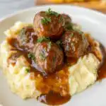 Close-up of Slow Cooker Salisbury Steak Meatballs in rich gravy served over creamy mashed potatoes, garnished with parsley.