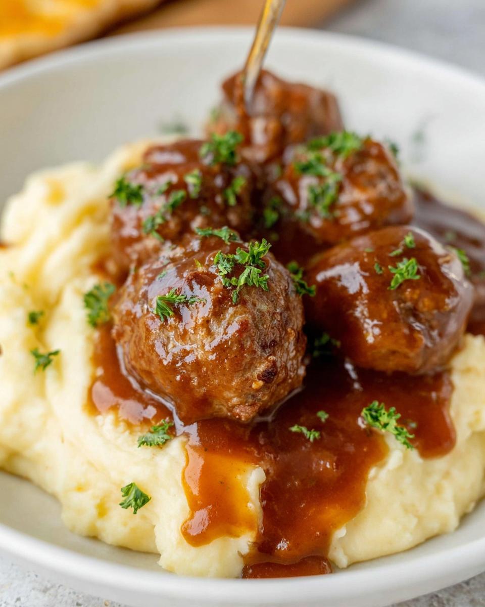 Close-up of Slow Cooker Salisbury Steak Meatballs served over creamy mashed potatoes and drizzled with rich gravy, garnished with parsley.