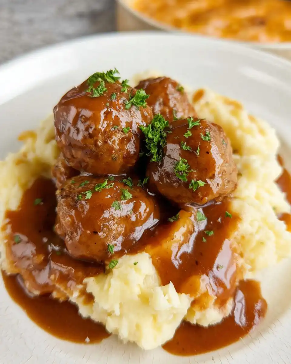 A plate of Slow Cooker Salisbury Steak Meatballs served over creamy mashed potatoes and smothered in rich brown gravy, garnished with parsley.