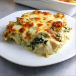 A delicious slice of spinach artichoke chicken casserole topped with melted, golden-brown cheese.