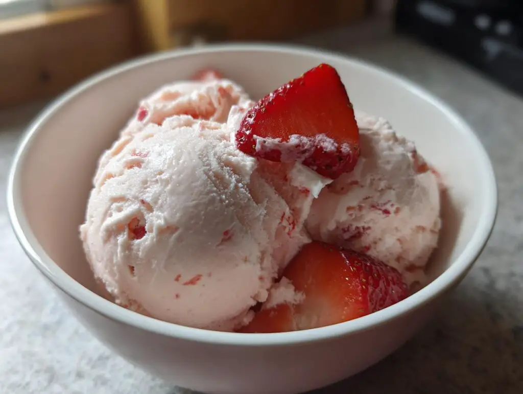 Close-up of creamy Strawberry Cottage Cheese Ice Cream with fresh strawberry slices in a white bowl.