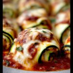 Close-up of Zucchini Rollatini with Ricotta and Marinara, baked with melted cheese and topped with fresh herbs.
