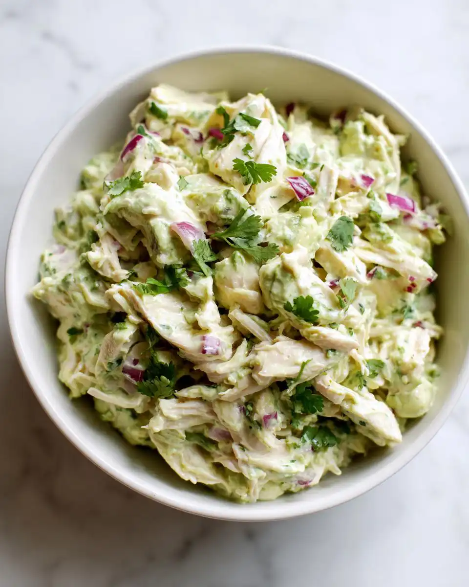 A close-up overhead view of a white bowl filled with 5-Minute Creamy Avocado Chicken Salad, garnished with fresh cilantro.