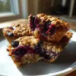 Close-up of Blueberry Baked Oatmeal Cups, showing a stack with one bitten into, revealing juicy blueberries and oats.