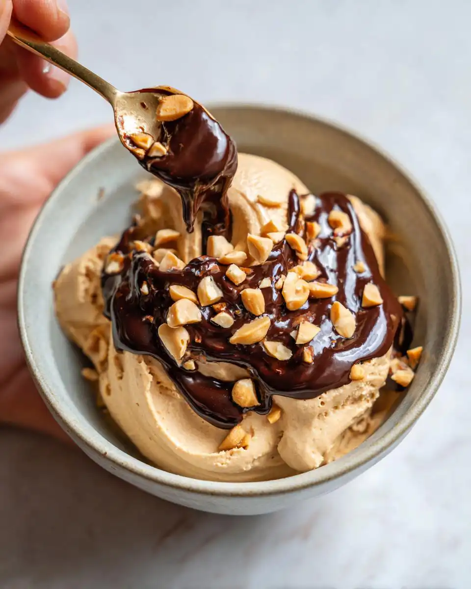 A spoonful of cottage cheese peanut butter mousse being lifted from a bowl, topped with chocolate sauce and chopped peanuts.