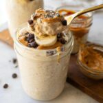 A spoonful of Creamy Blended Overnight Oats High Protein Easy Breakfast topped with peanut butter, chocolate chips, chia seeds, and banana slices.