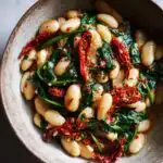 Close-up of Creamy Tuscan Marry Me Butter Beans with wilted spinach and sun-dried tomatoes in a rustic bowl.