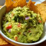 Close-up of a bowl of fresh Easy Appetizer Guacamole with Tortilla Chips, featuring chunks of avocado, tomato, red onion, and cilantro.