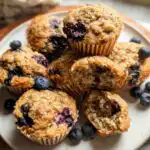 A plate of Healthy Blueberry Banana Protein Muffins, some whole and one broken in half to show the moist interior and blueberries.