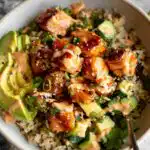 A close-up of a delicious bowl filled with Honey Glazed Salmon Bowls, brown rice, avocado slices, and cucumber.