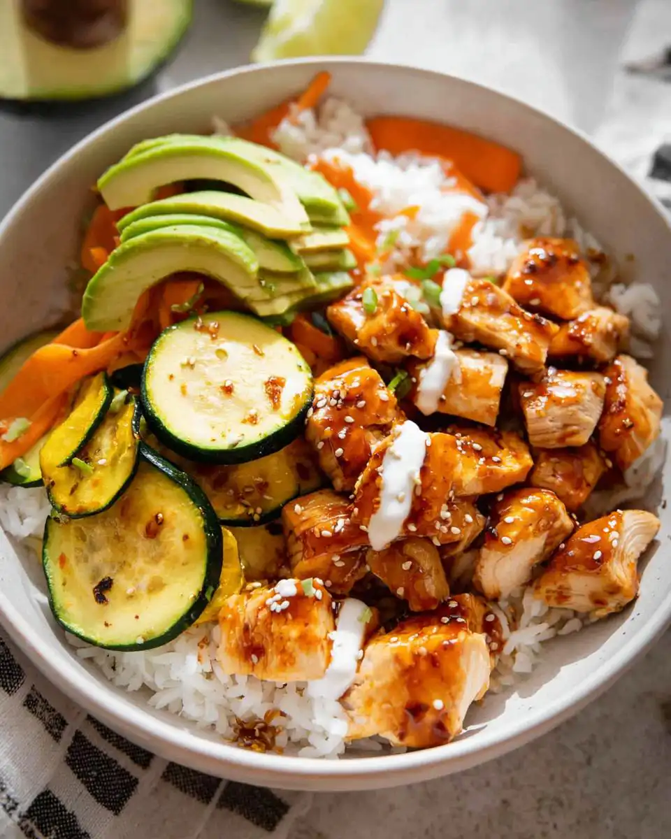 A delicious bowl of Hot Honey Chicken and Rice with sliced avocado, zucchini, and carrots.