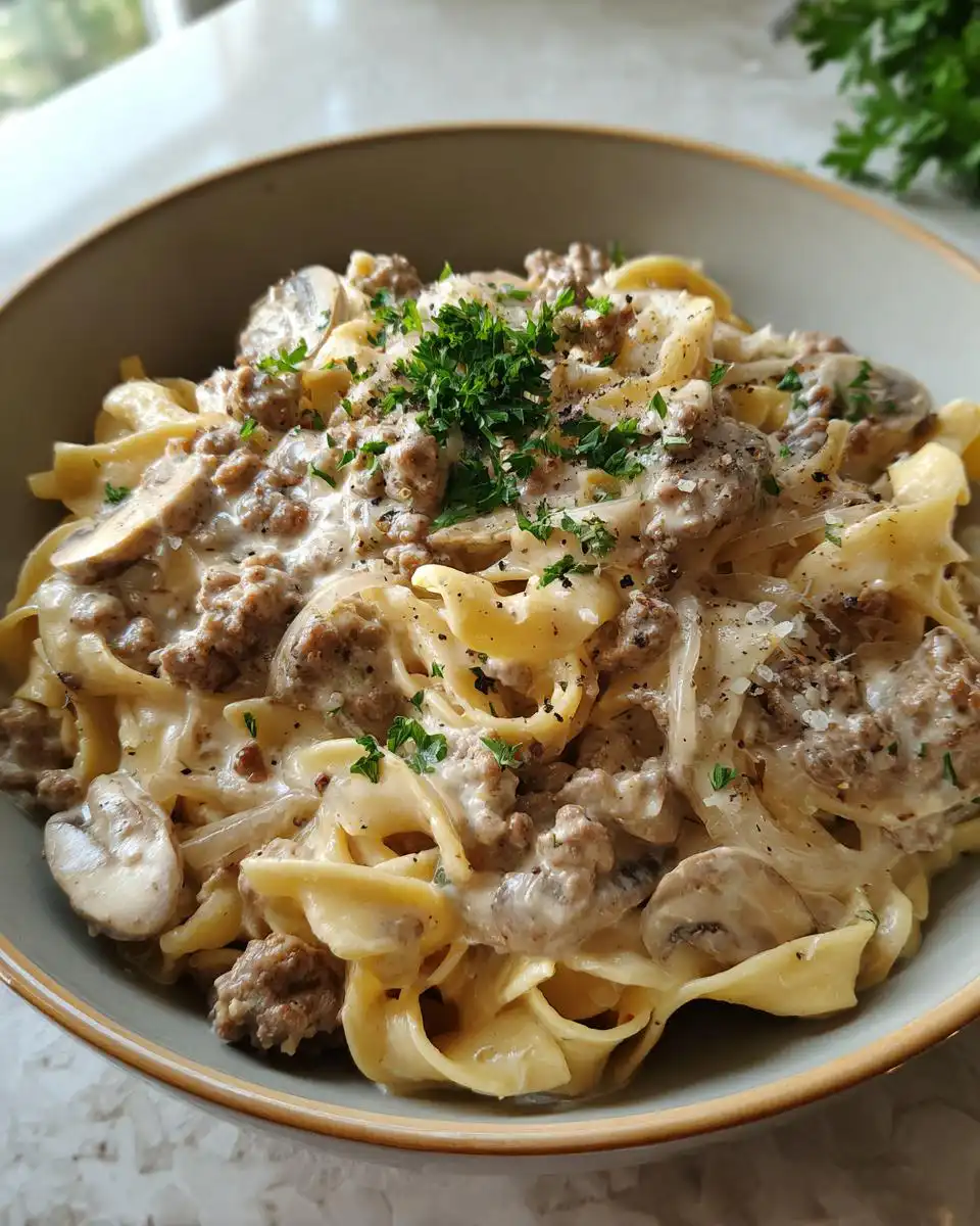 A close-up of a bowl of instant pot beef stroganoff, featuring wide egg noodles, ground beef, mushrooms, and a creamy sauce, garnished with fresh parsley.