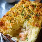 A close-up of a golden-brown, mashed potato topped fish pie, revealing creamy filling with prawns and peas, a perfect Mary Berry fish pie recipe.