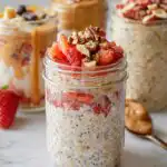 A close-up of Mary Berry overnight oats in a jar, topped with fresh strawberries and chopped nuts.