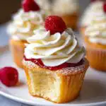 A delicious Mary Berry Victoria Sponge cupcake with a bite taken out, topped with cream and a raspberry.