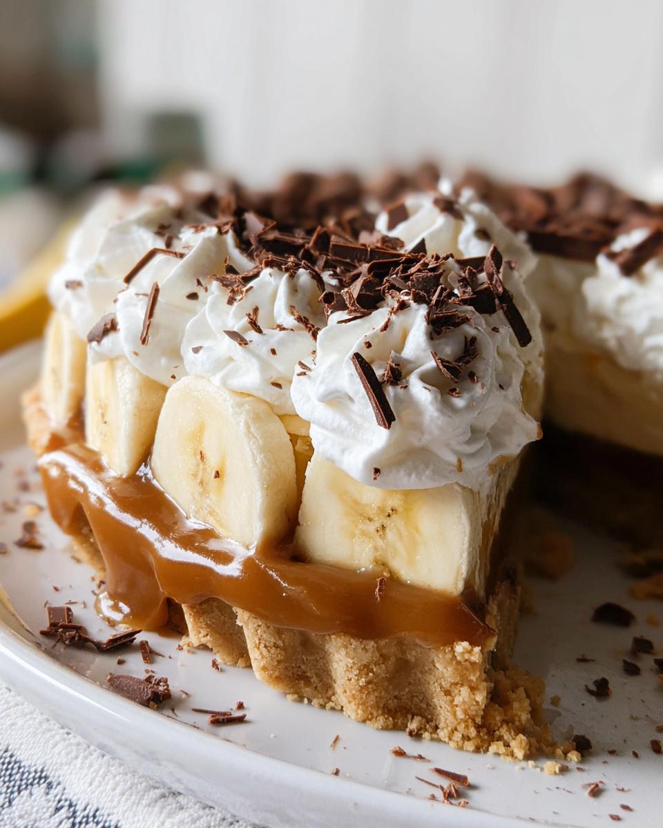A delicious slice of Banoffee Pie inspired by Mary Berry, featuring a biscuit base, caramel, banana slices, whipped cream, and chocolate shavings.