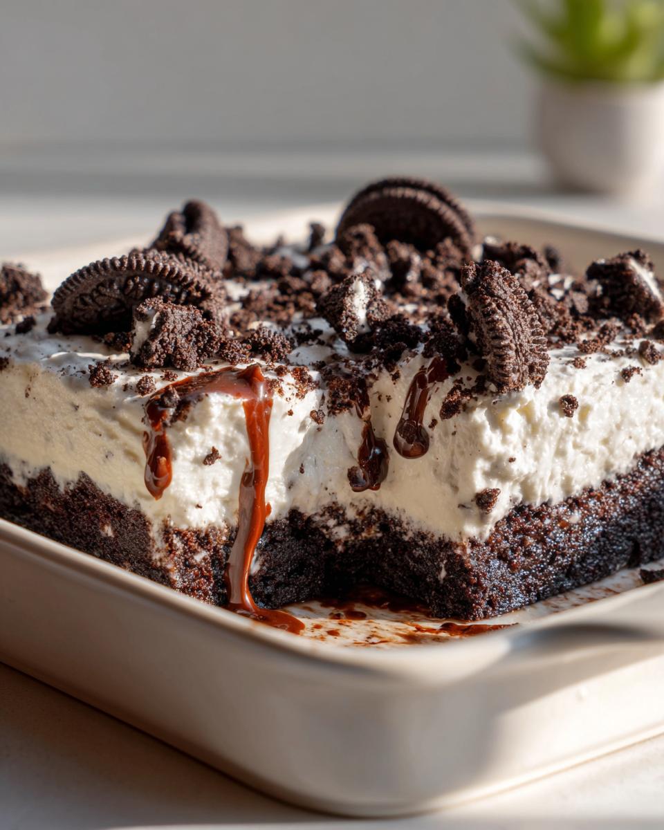 A close-up of a slice of easy Oreo dessert bars, topped with whipped cream, crushed Oreos, and chocolate drizzle.
