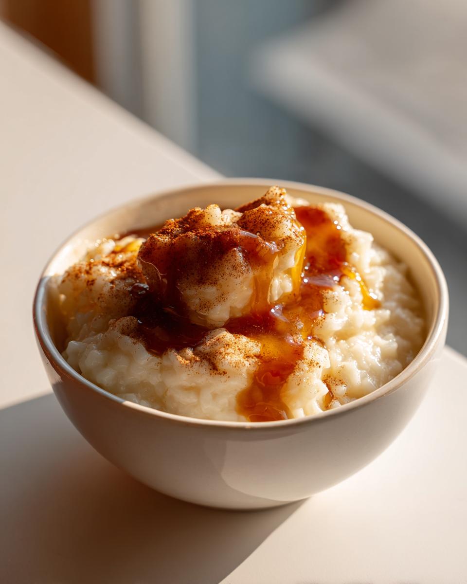 A close-up of a bowl of creamy easy vegan rice pudding, topped with cinnamon and a drizzle of syrup.