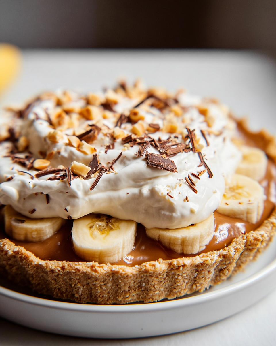 Close-up of a delicious Mary Berry-inspired Banoffee Pie, featuring a biscuit base, caramel, banana slices, whipped cream, chocolate shavings, and chopped nuts.
