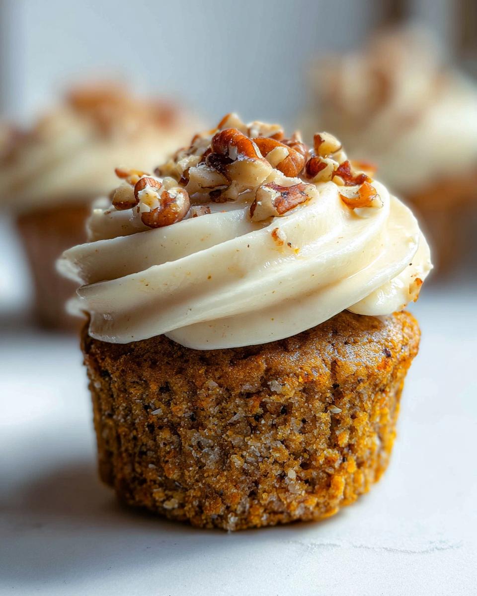 Close-up of a delicious Mary Berry-Inspired Easy Carrot Cake Cupcake topped with cream cheese frosting and chopped nuts.