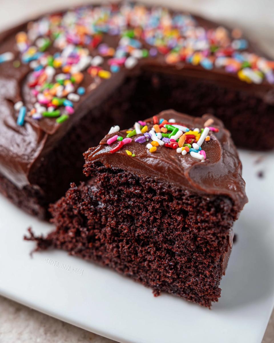 A slice of single layer chocolate cake inspired by Mary Berry, topped with chocolate frosting and colourful sprinkles.