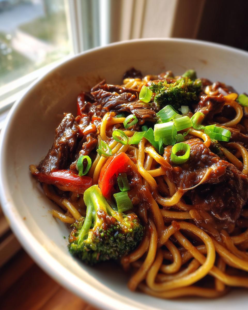 A bowl of Mongolian beef noodle stir fry with tender beef, noodles, broccoli, and red peppers, garnished with green onions.