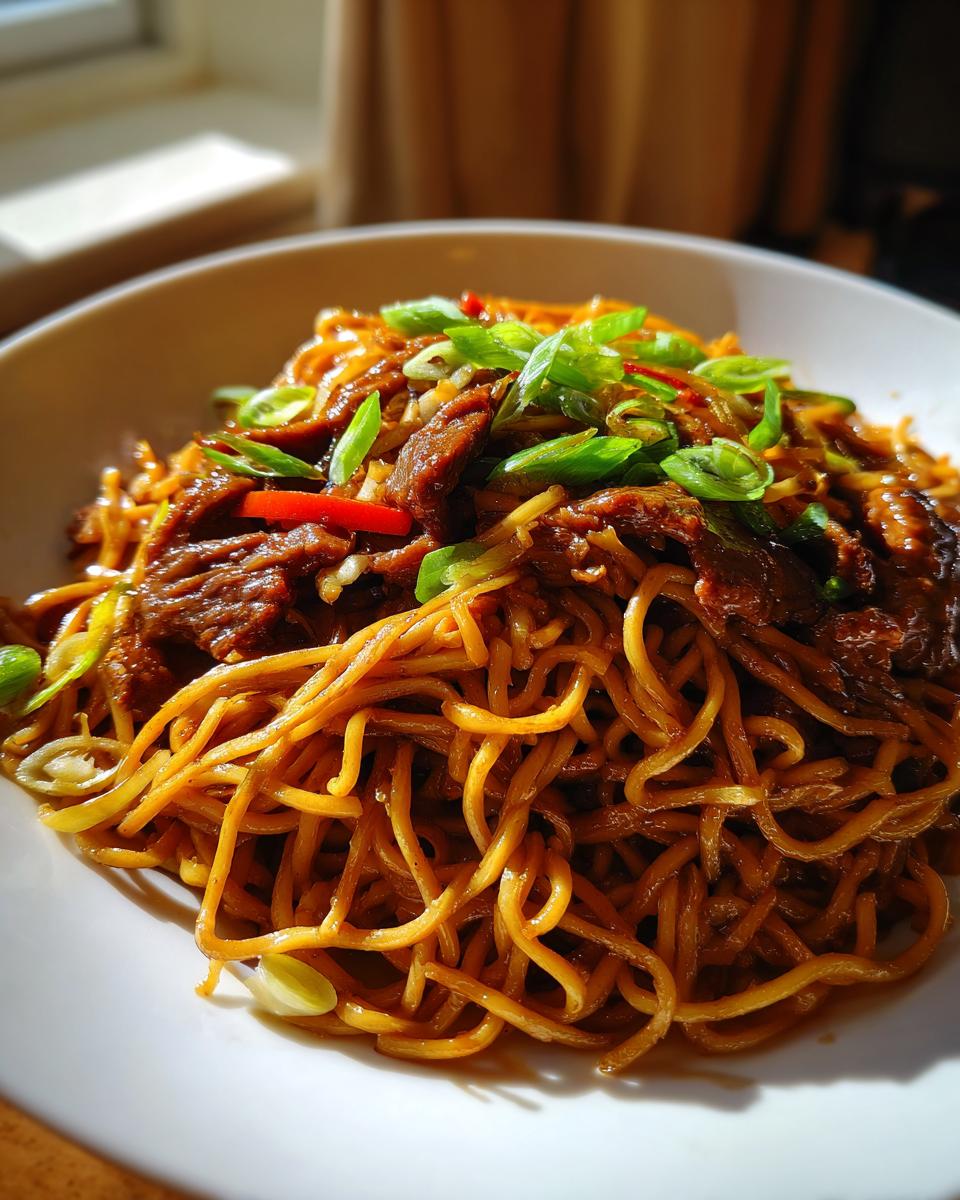 A close-up view of a bowl of Mongolian Beef Noodles, featuring tender beef strips and savory noodles topped with green onions.