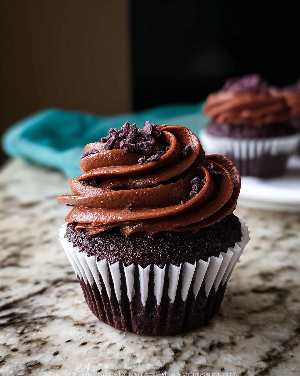 A close-up of a decadent Nigella Lawson inspired chocolate cupcake with rich chocolate frosting and purple sprinkles.
