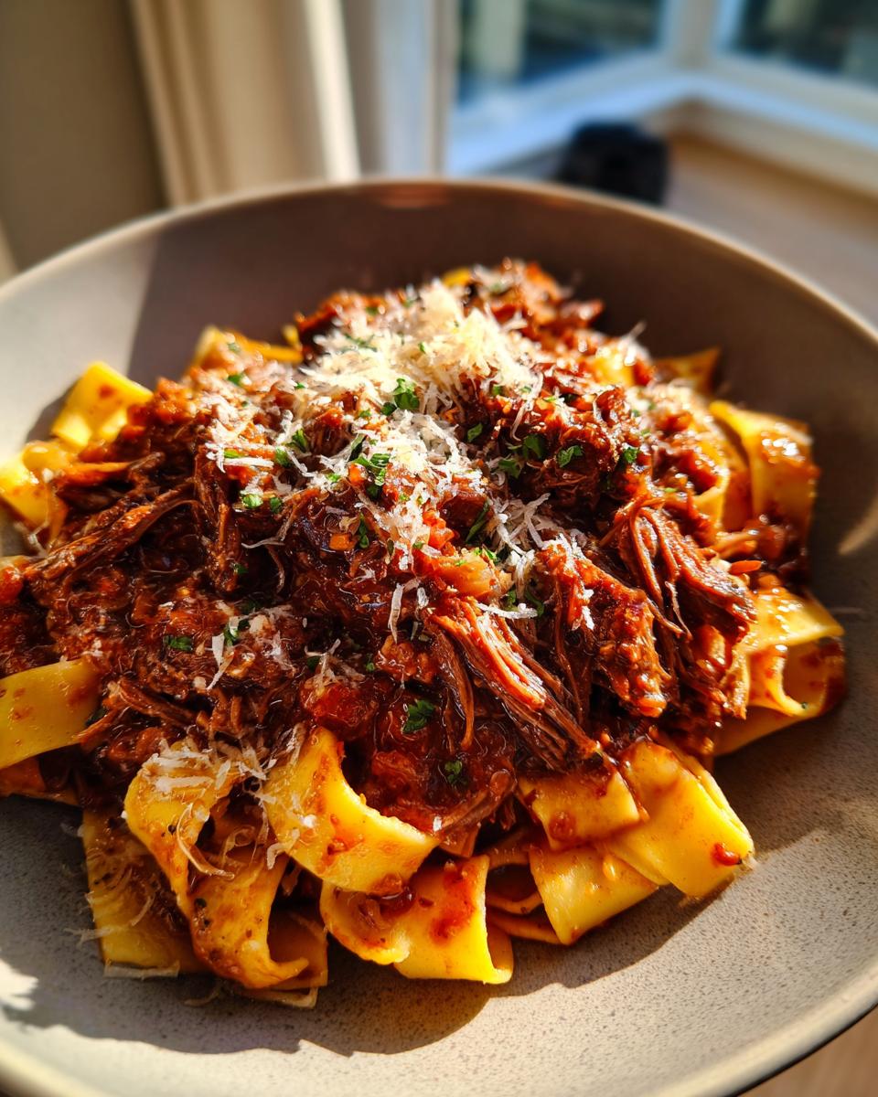 A bowl of pappardelle pasta topped with rich short rib ragu and grated Parmesan cheese.