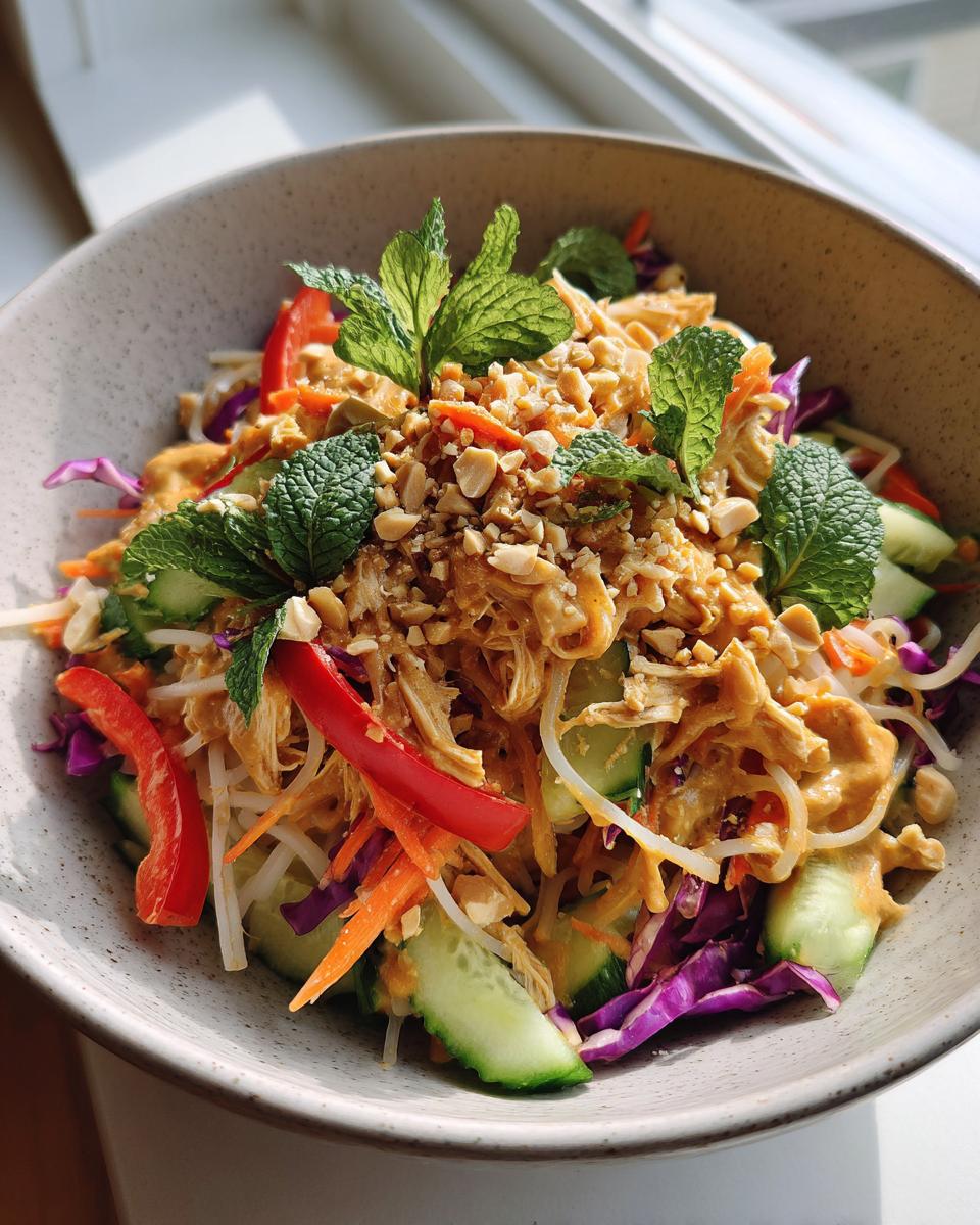 A vibrant spring roll salad bowl with shredded chicken, cucumber, carrots, red cabbage, red pepper, and mint, topped with crushed peanuts and peanut dressing.