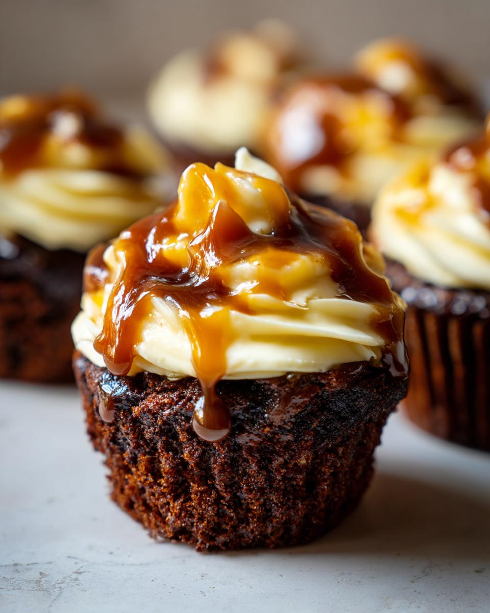 Close-up of a moist sticky toffee cupcake topped with creamy frosting and a generous drizzle of caramel sauce.